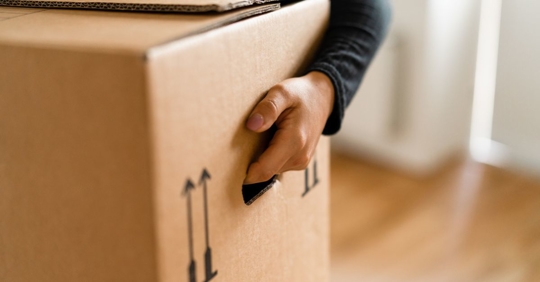 A woman is carrying cardboard moving boxes into her new apartment.